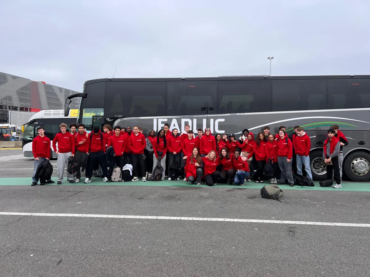 Groupe d'élèves BRILLA en sweats rouges devant le car au départ de Belgique
